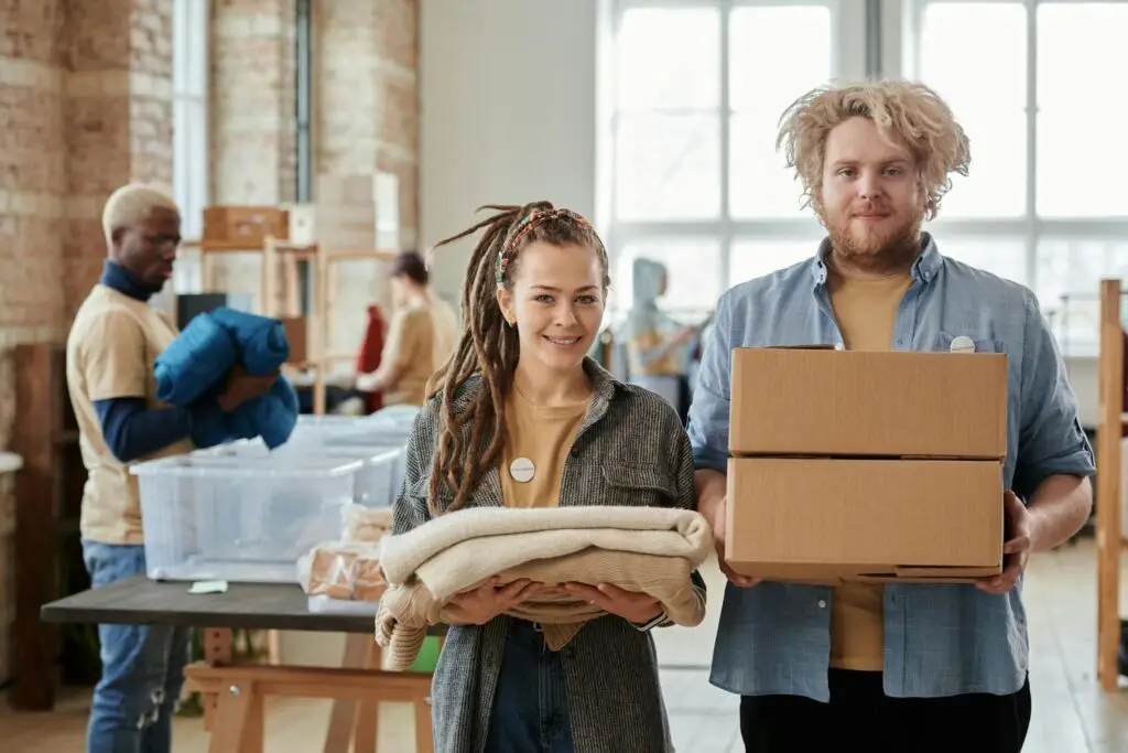 Smiling volunteers holding boxes and clothes, assisting in a donation drive indoors.